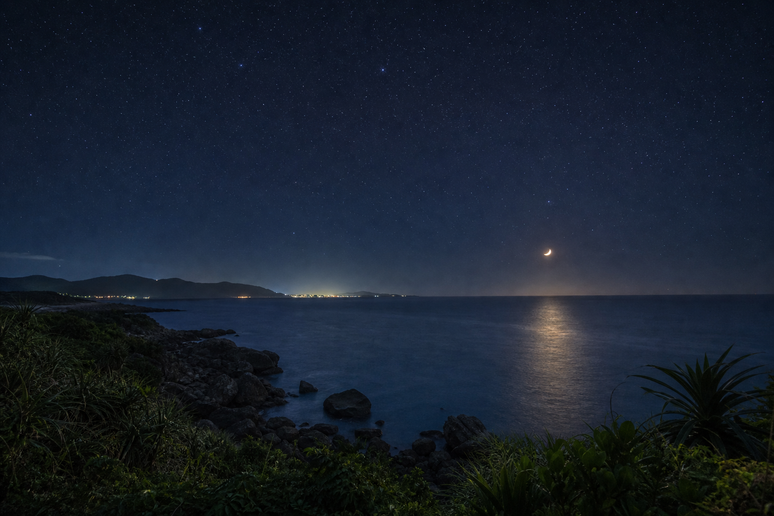 沖縄北部の静かな海岸を陸上から望む、三日月と星が見える夜空